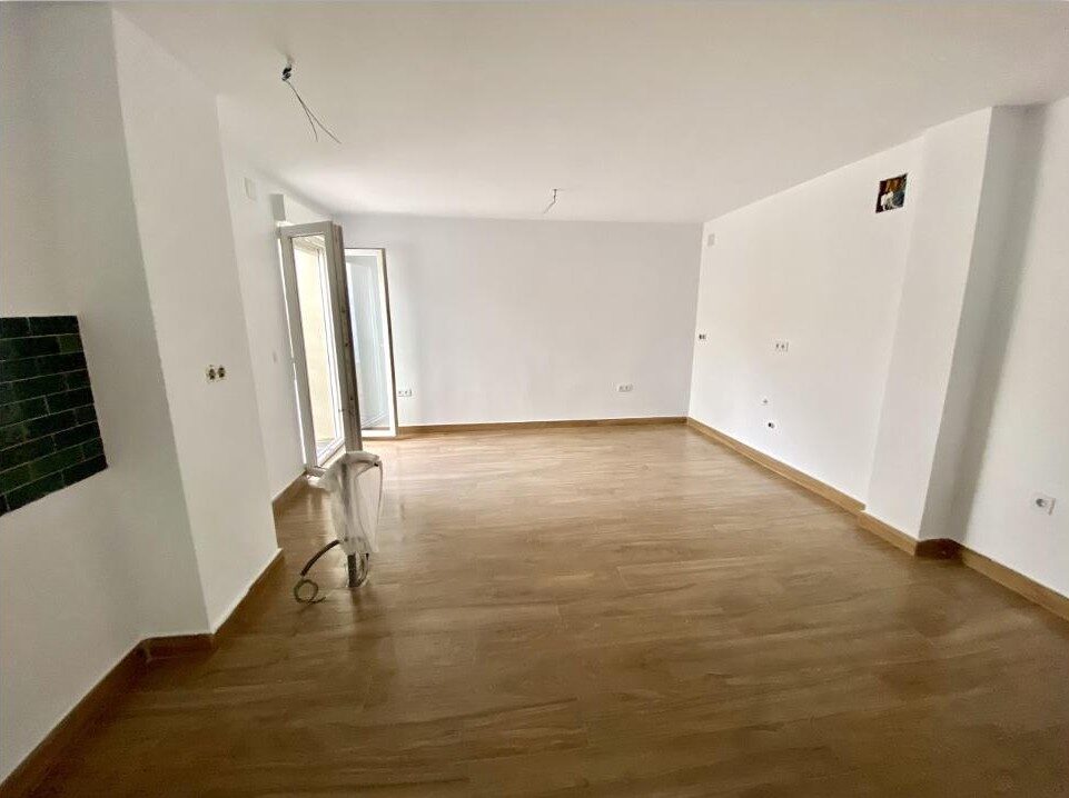Salón reformado con suelo de madera acabado, paredes blancas y puerta de acceso a terraza